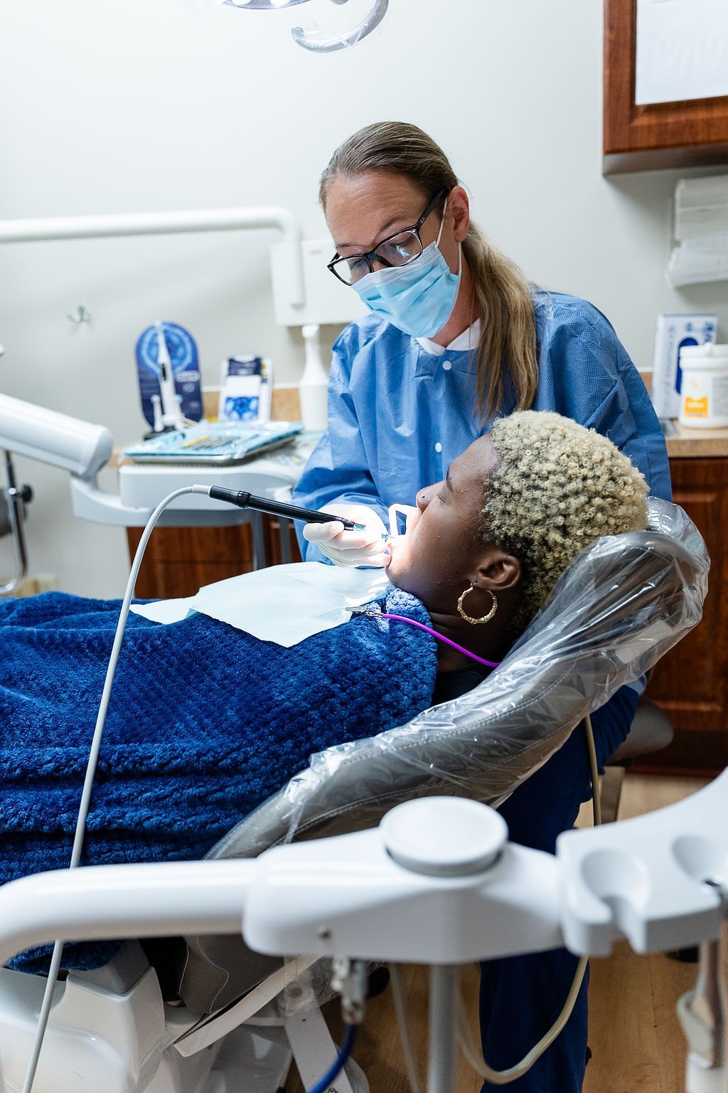 Dentist wearing a mask examines a patient reclined in a dental chair