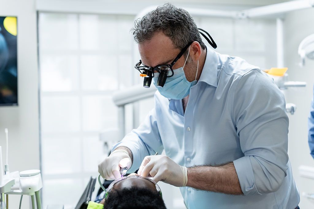 Dentist wearing magnifying glasses treats a patient in a bright clinic