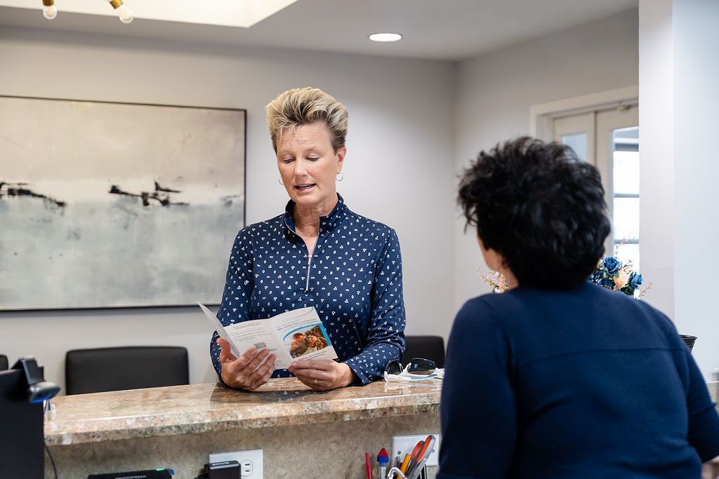 Two people talking at a reception desk in a bright office lobby