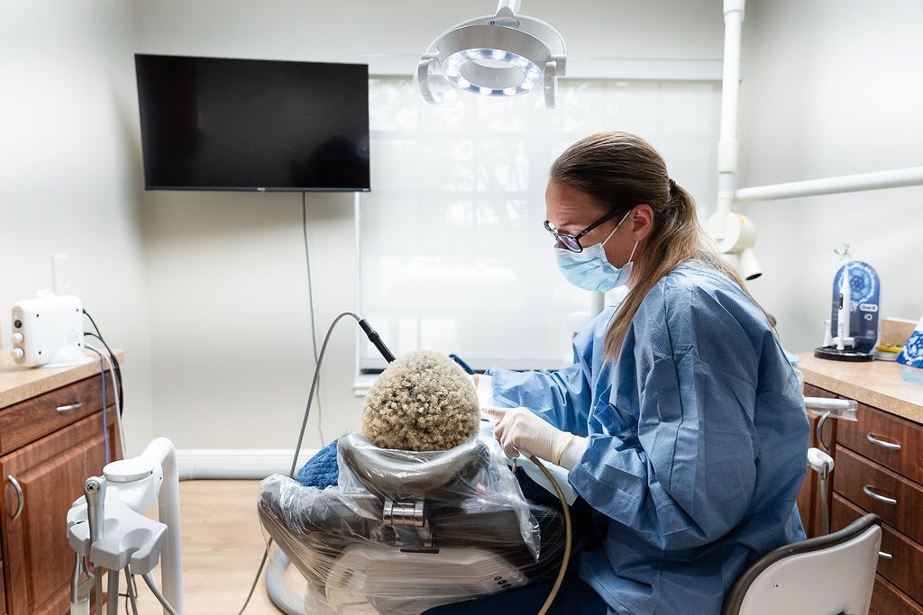 Dentist treating a patient in a bright dental clinic, with a TV on the wall and a dental chair.