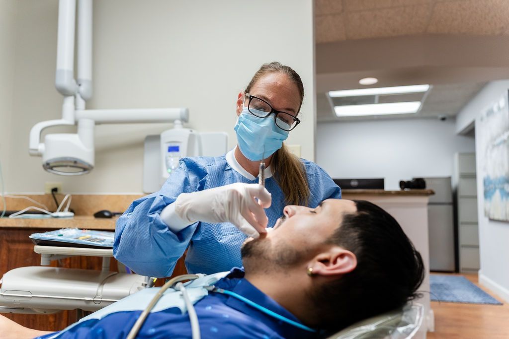 Dentist in blue scrubs examines a reclining patient in a dental clinic