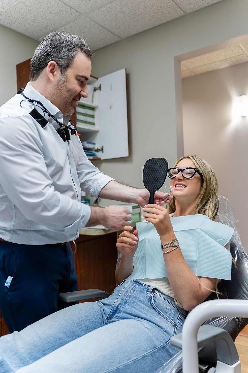 Dentist examining a smiling patient in a chair, holding a dental mirror