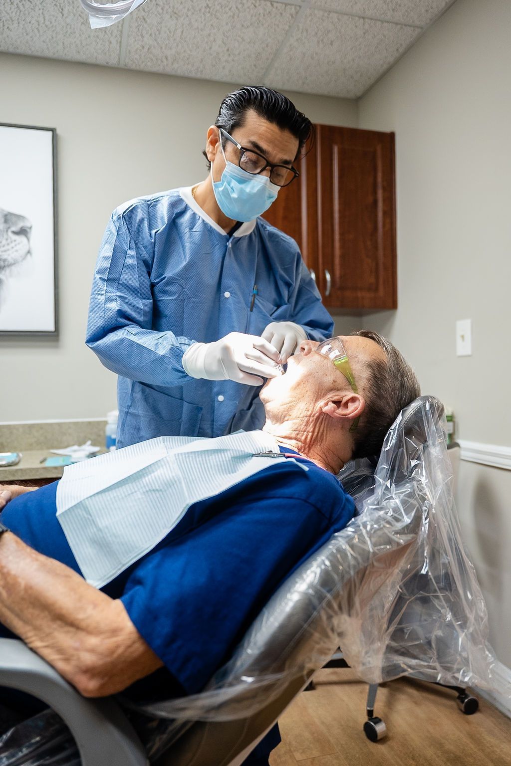 Dentist examining a patient in a reclining chair with a blue bib in a clinic.