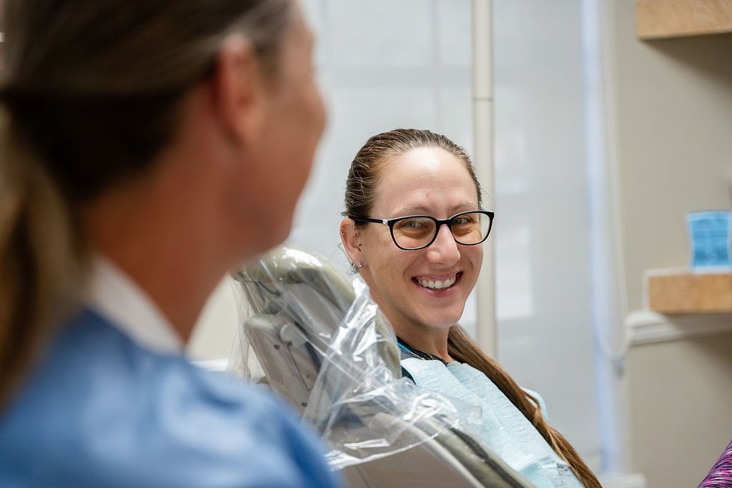 Patient smiling in a dental chair while speaking with a clinician nearby