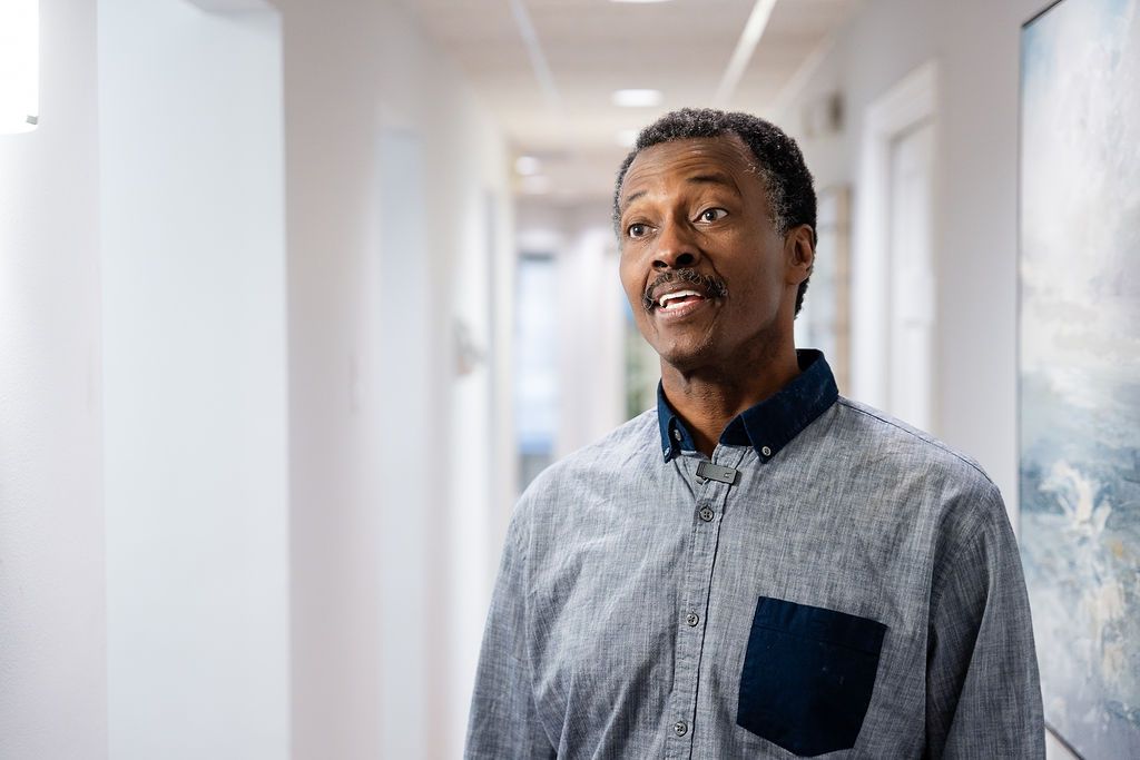 Man standing in a bright hallway, wearing a light blue shirt
