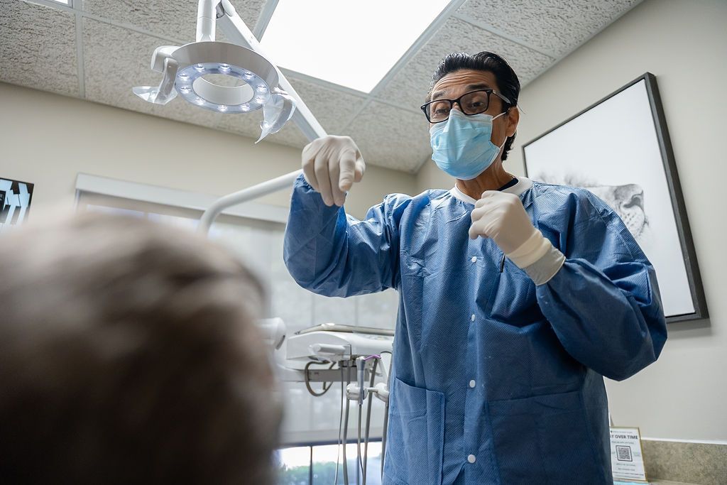 Dentist in blue protective gear and mask preparing tools in a dental exam room