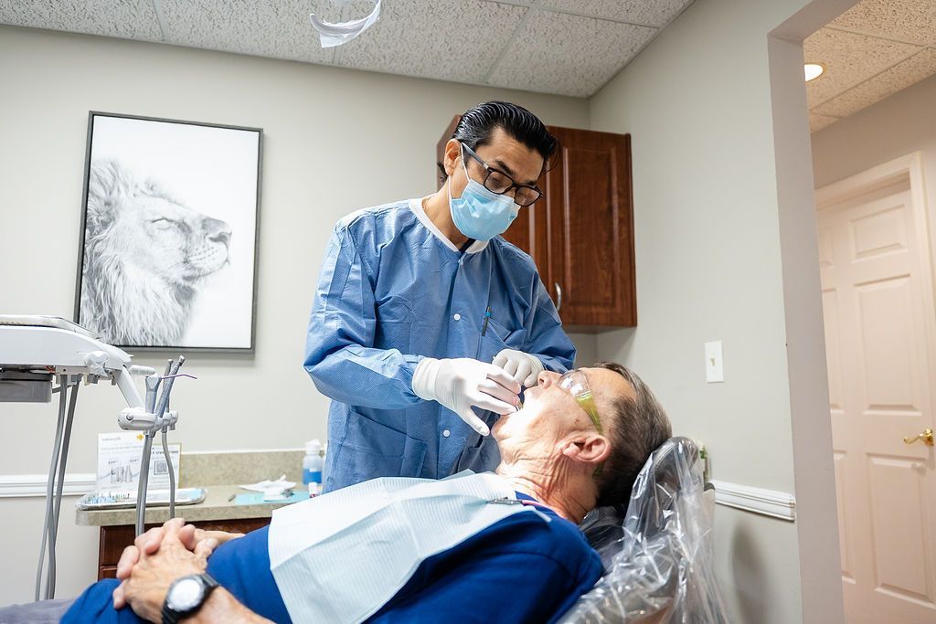 Dentist treating a reclined patient in a dental office, wearing mask and gloves