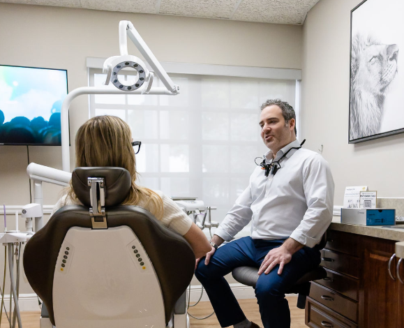 Dentist consulting a patient in a bright exam room, with dental chair and overhead light.