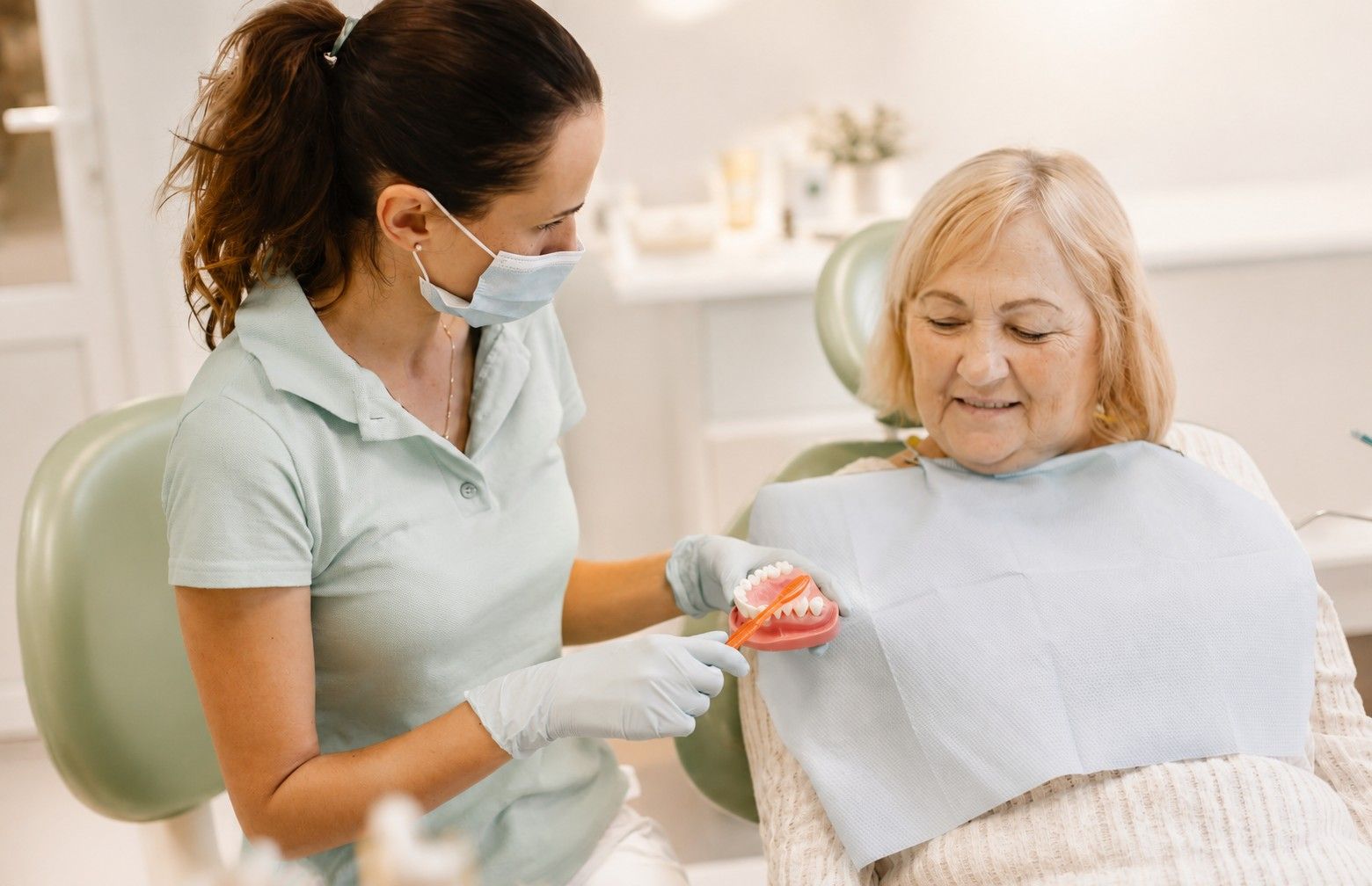 Dental hygienist showing denture to elderly patient in a bright clinic