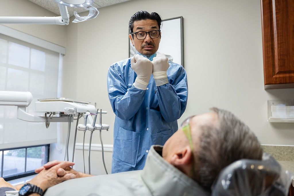 Dentist in blue scrubs and gloves preparing to treat a reclining patient