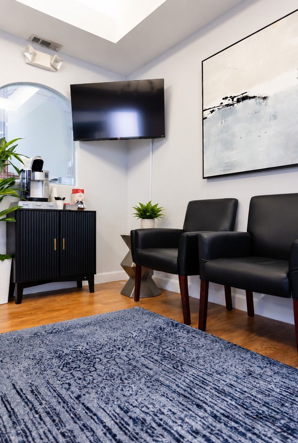 Modern waiting room with black chairs, wall-mounted TV, abstract art, and blue rug
