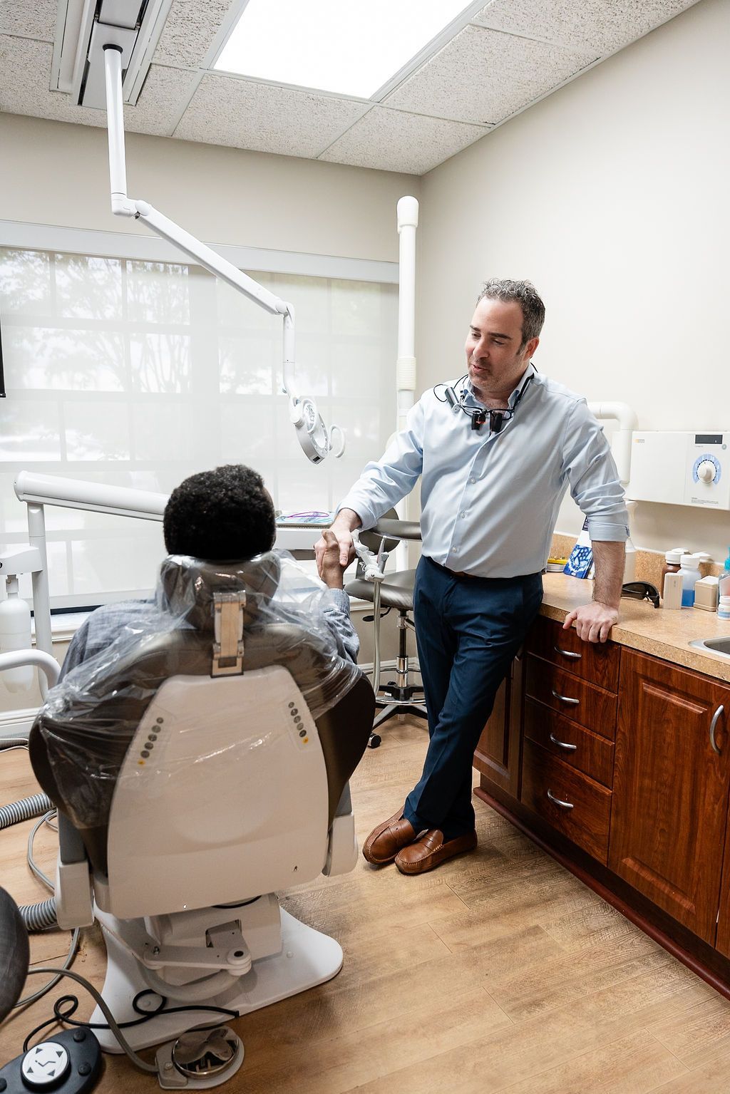 Dentist speaking with a patient seated in a dental chair inside a treatment room