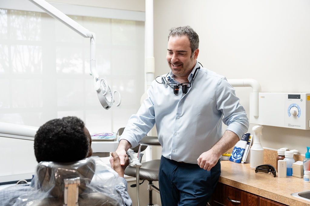 Dentist smiling at a patient in a bright exam room, with dental tools and supplies nearby