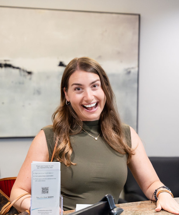 Woman smiling behind a reception desk with a QR code sign