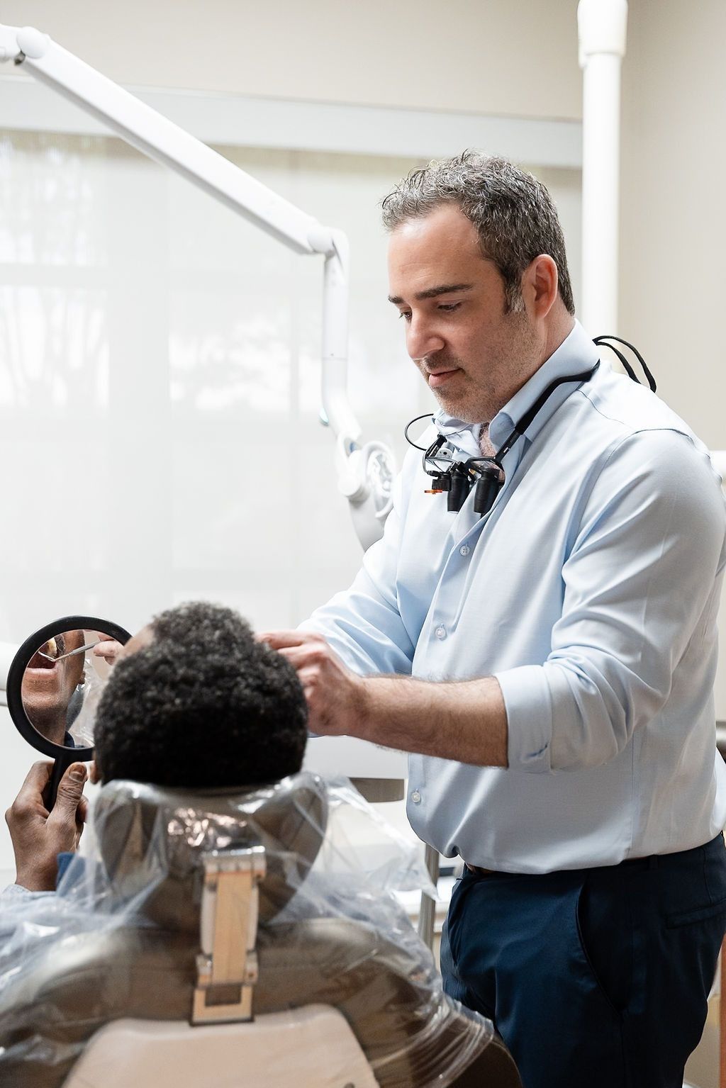 Dentist examining a patient in a dental chair, using a mirror in a bright clinic.