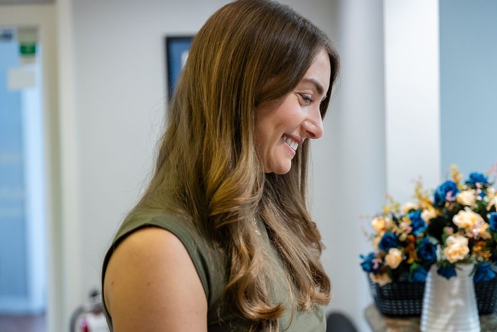 Woman smiling in profile beside a vase of blue and white flowers indoors