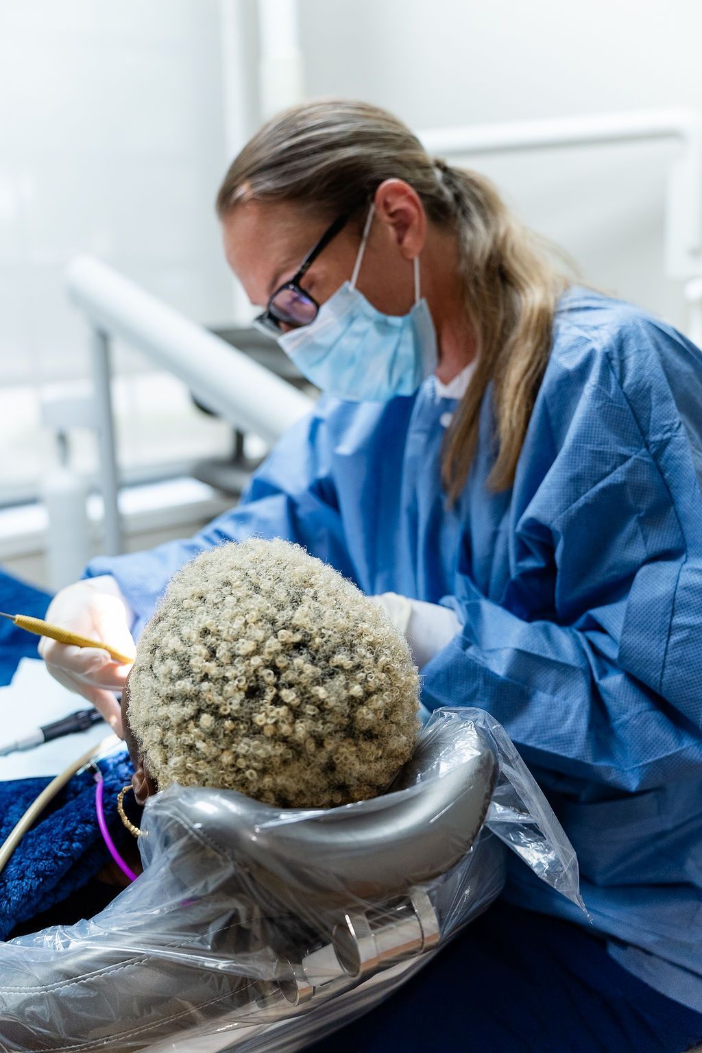 Dentist in blue protective gear examining a patient during a dental procedure