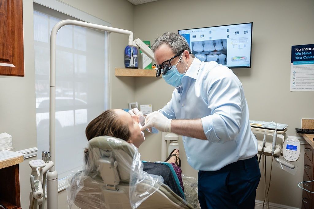 Dentist treating a patient in a dental chair, with a monitor and dental tools in a bright clinic.
