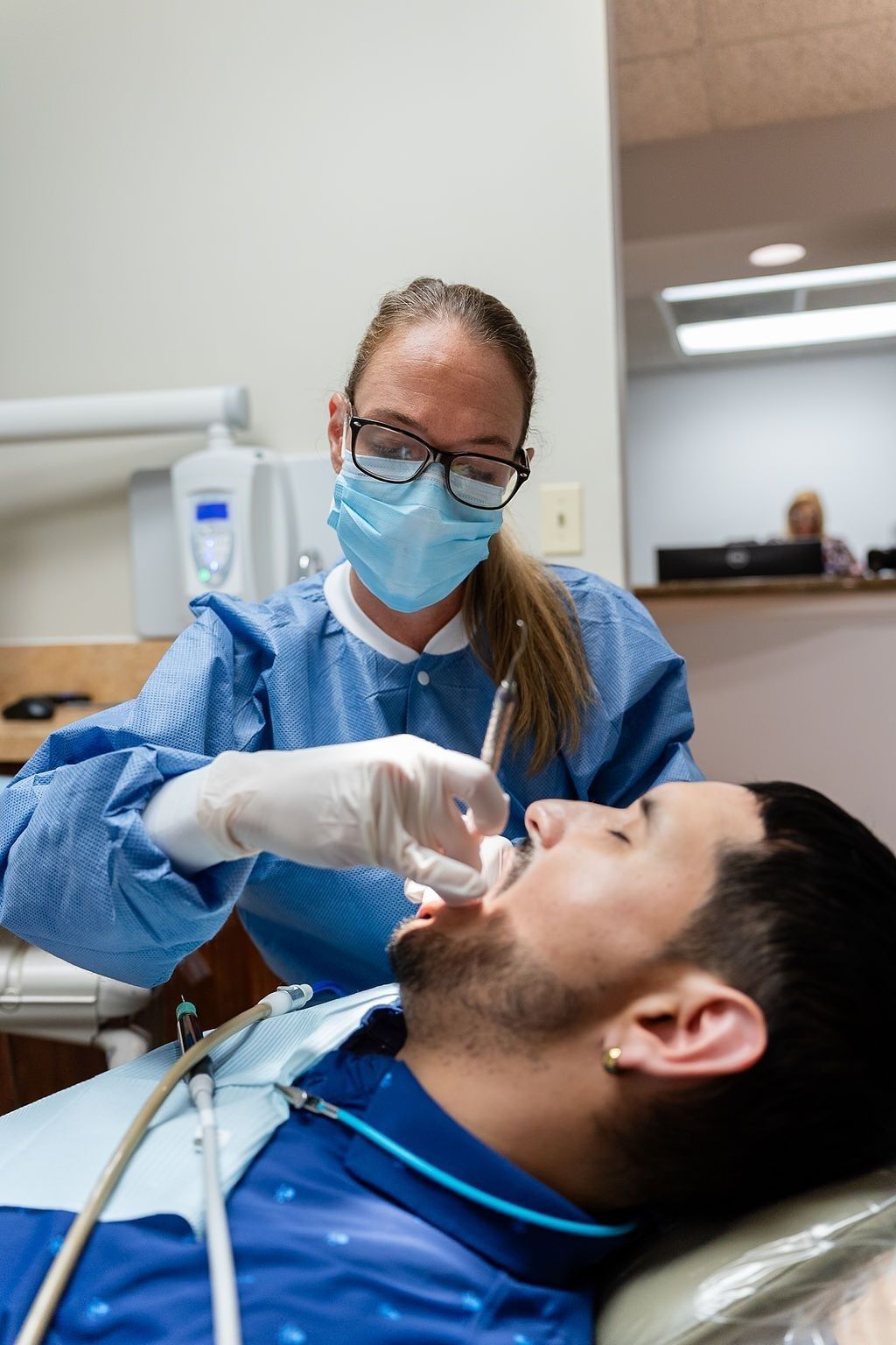 Dentist wearing a mask and gloves examines a patient in a dental chair.
