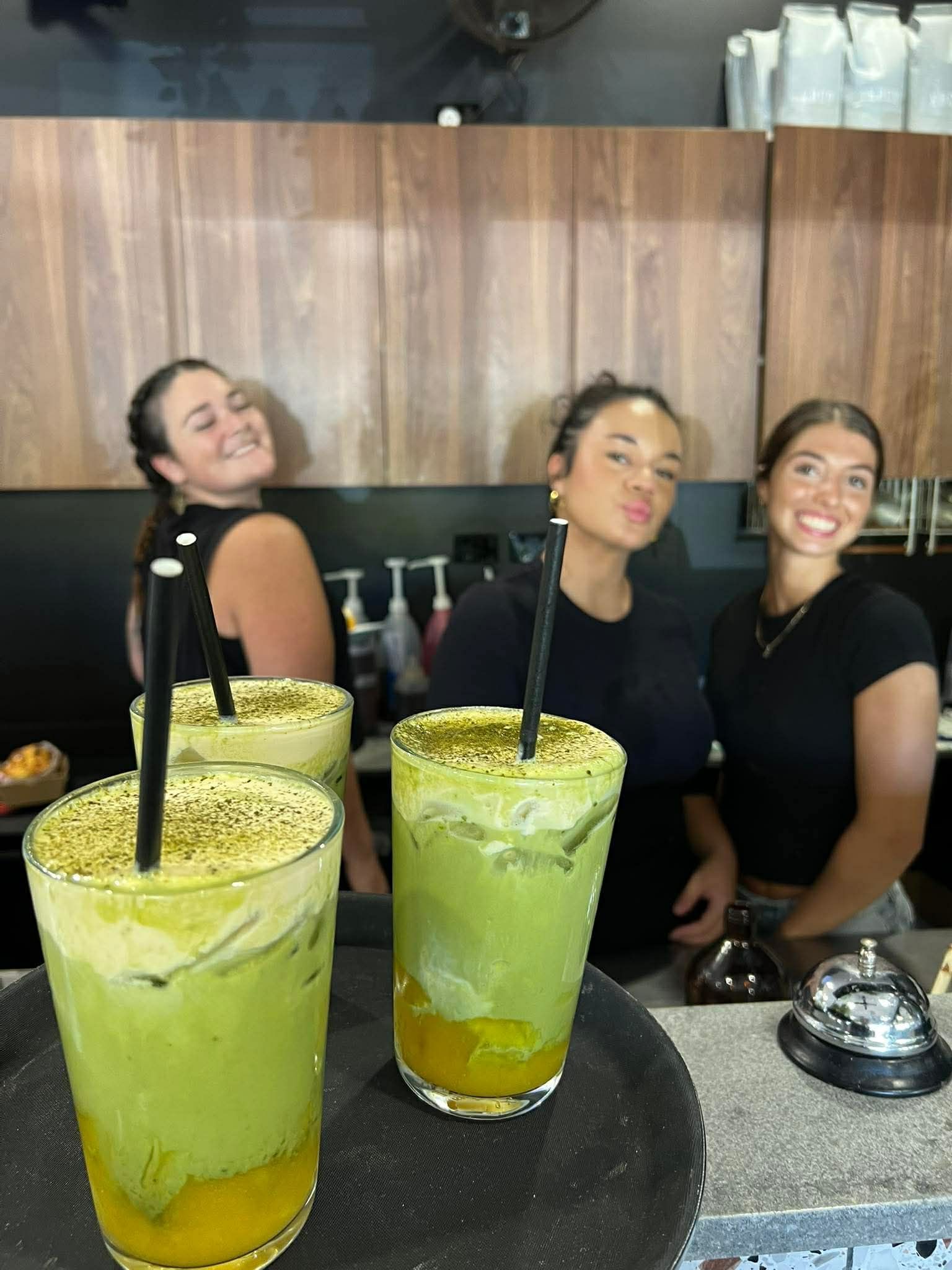 Three team members smiling behind their tray of drinks for customers of the cafe