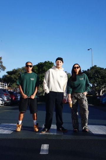 Group of three people wearing the merchandise from the brand of green and cream jumpers and tshits