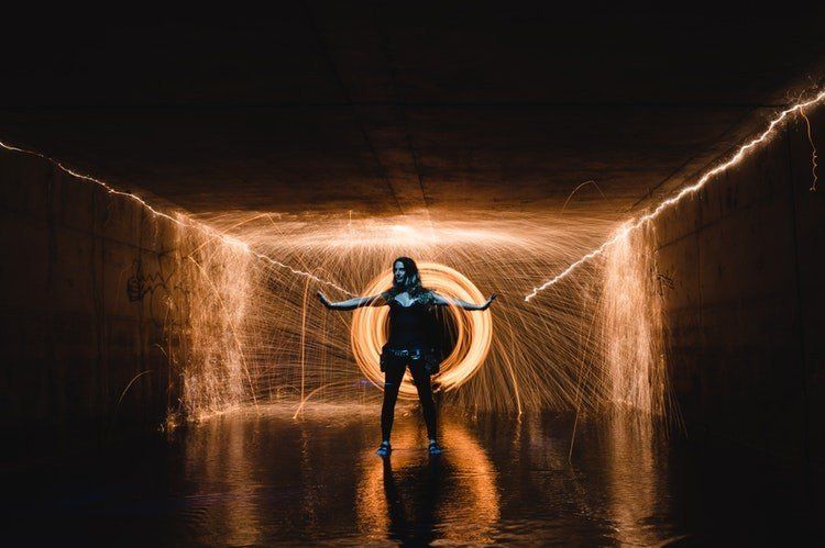 Person standing in a glowing tunnel, surrounded by warm orange light and reflections on the floor