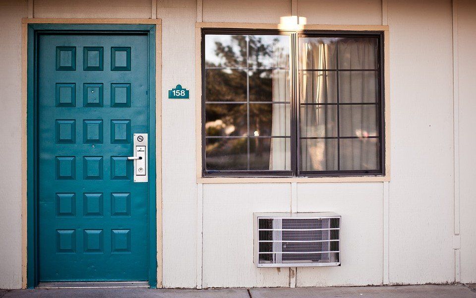 Teal door beside a window with an air conditioner in a white exterior wall