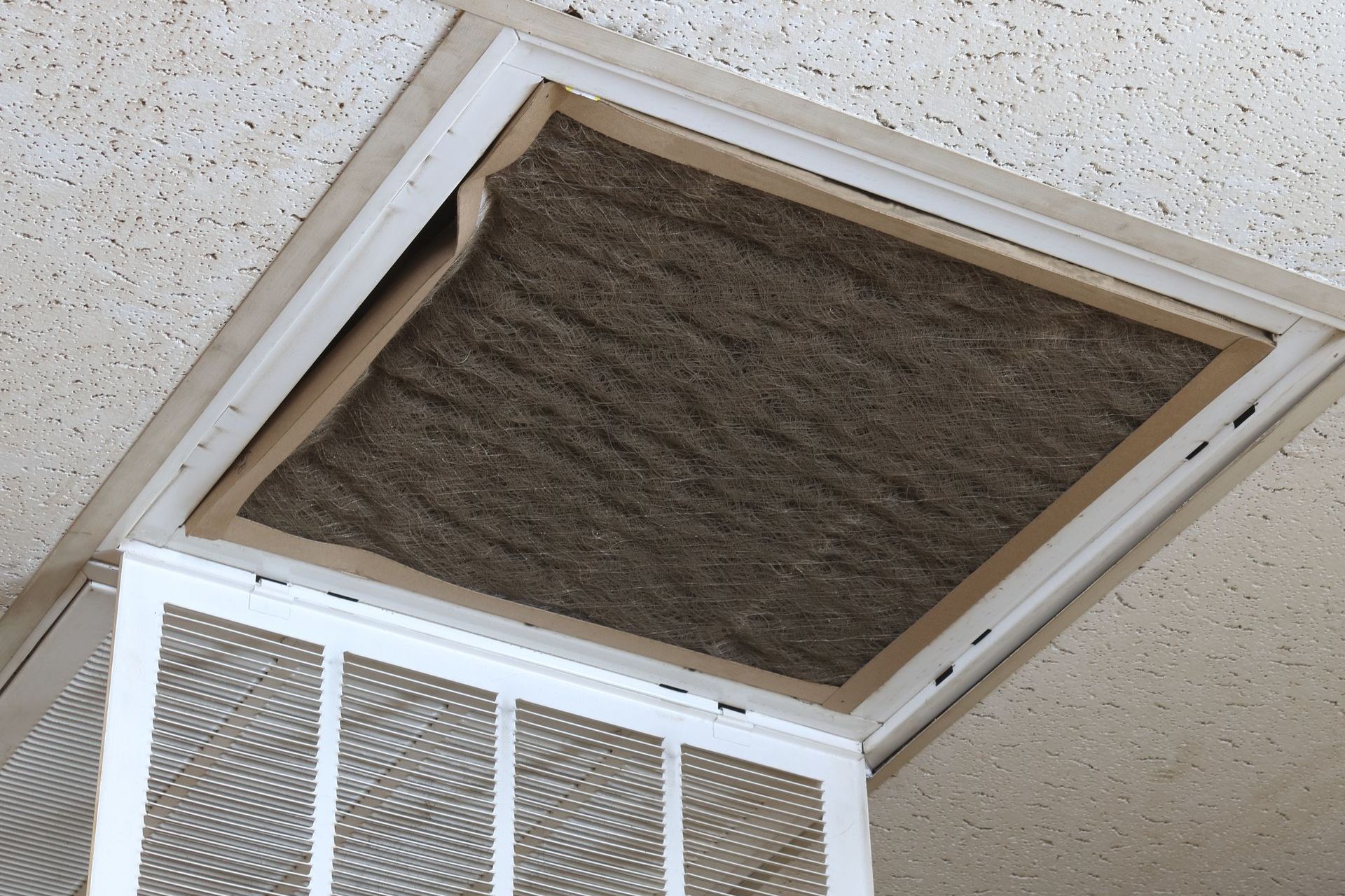 Grille d'aération au plafond avec filtre brun sale.