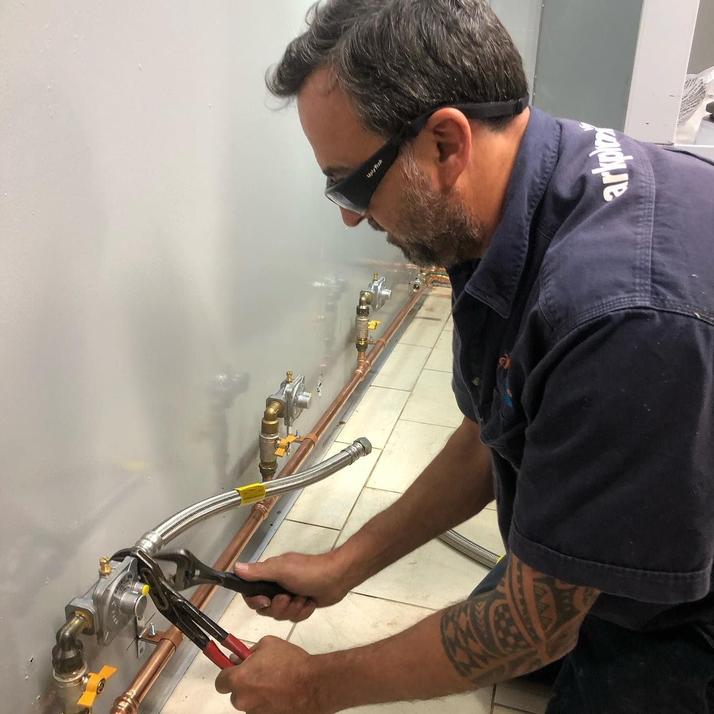 A Man Is Working On A Pipe With A Pair Of Pliers — ARK Plumbing & Gasfitting In Exeter, NSW