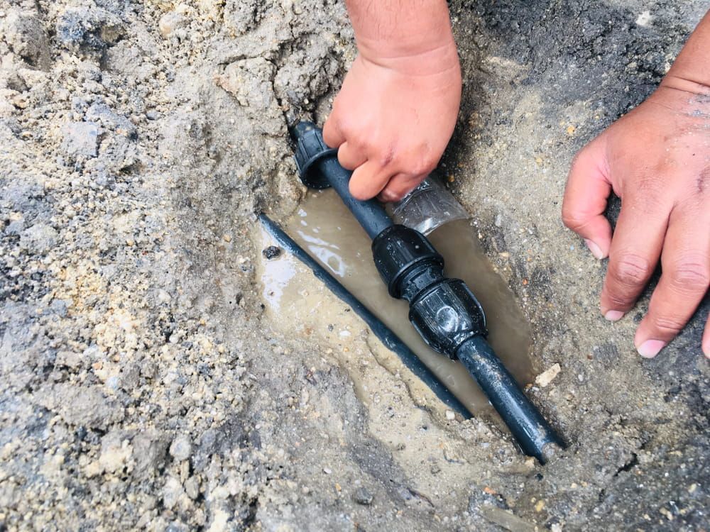 A Person Is Fixing A Broken Pipe In The Dirt — ARK Plumbing & Gasfitting In Berrima, NSW