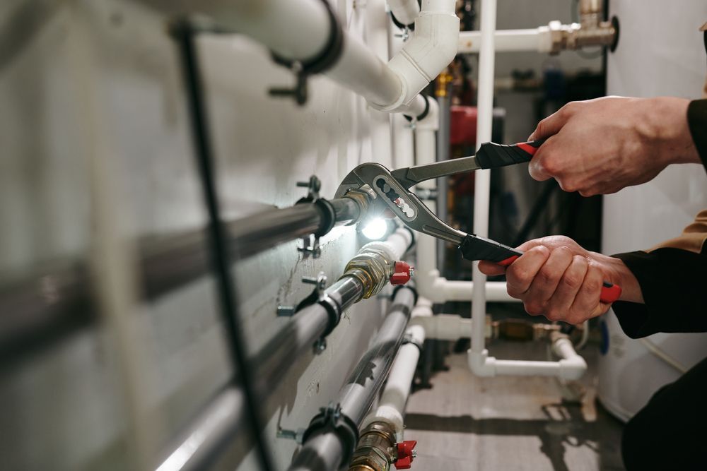 A Plumber Is Working On A Pipe With A Wrench — ARK Plumbing & Gasfitting In Bowral, NSW