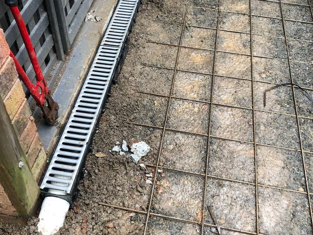 A Drain Is Being Installed On The Ground Next To A Brick Wall — ARK Plumbing & Gasfitting In Exeter, NSW