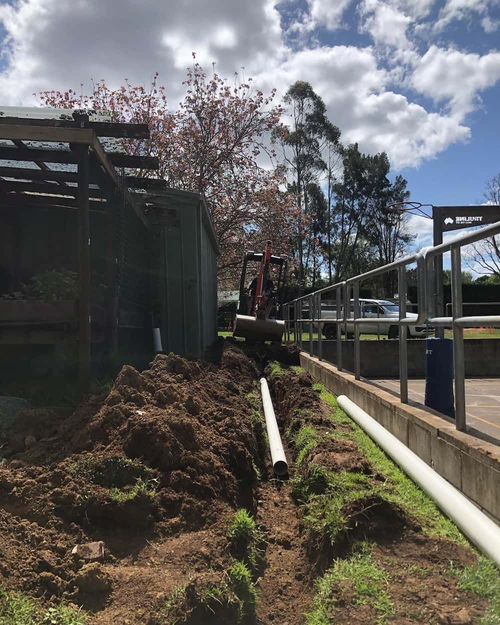 A Bulldozer Is Digging A Hole In The Ground Next To A Fence — ARK Plumbing & Gasfitting In Exeter, NSW