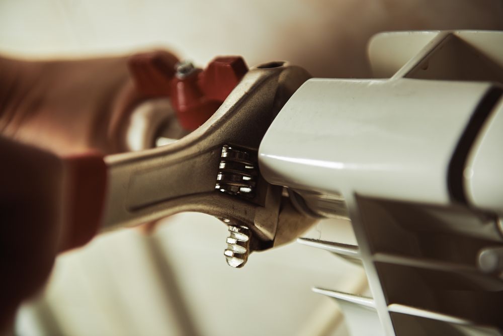 A Person Is Fixing A Radiator With A Wrench β ARK Plumbing & Gasfitting In Moss Vale, NSW