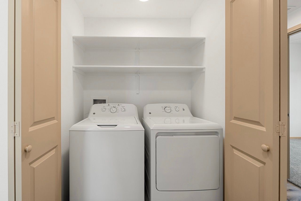 In-unit laundry closet with a white top-loading washer, a front-loading dryer, and shelves above.