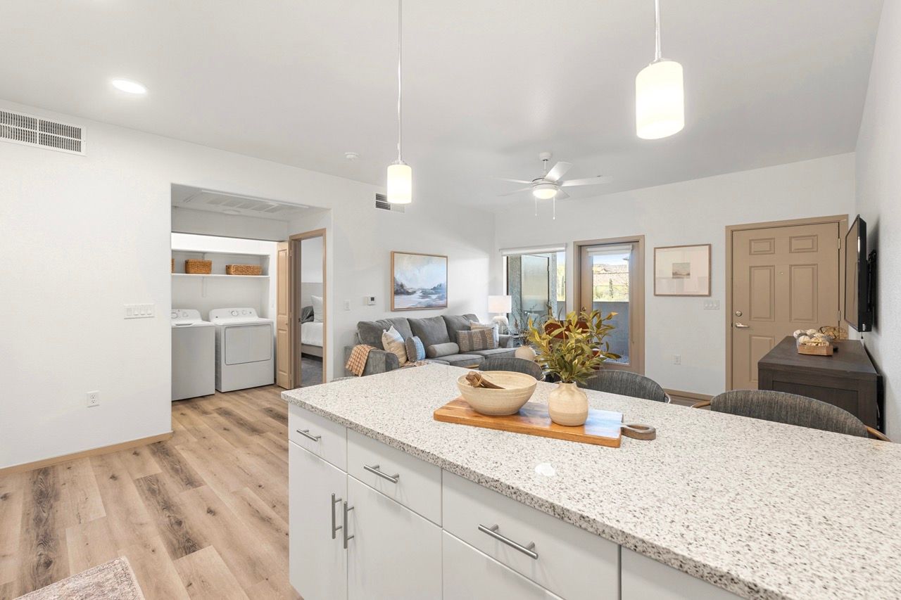 Open-concept apartment kitchen and living area with island; laundry area visible in the back.