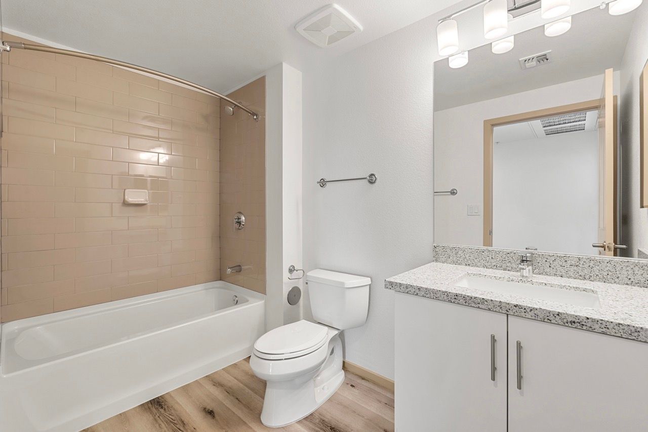 Bathroom with a bathtub/shower, beige tile surround, toilet, and granite vanity.