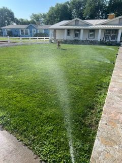 Sprinkler spraying water across a green lawn beside a stone walkway and house