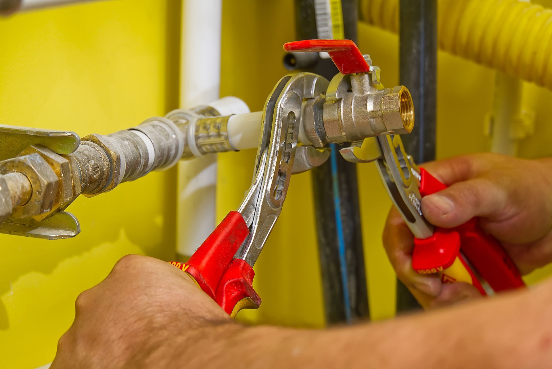 A person is fixing a pipe with a wrench and pliers.