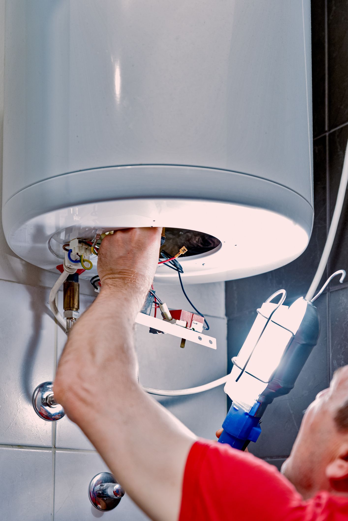 A man is fixing a water heater in a bathroom.