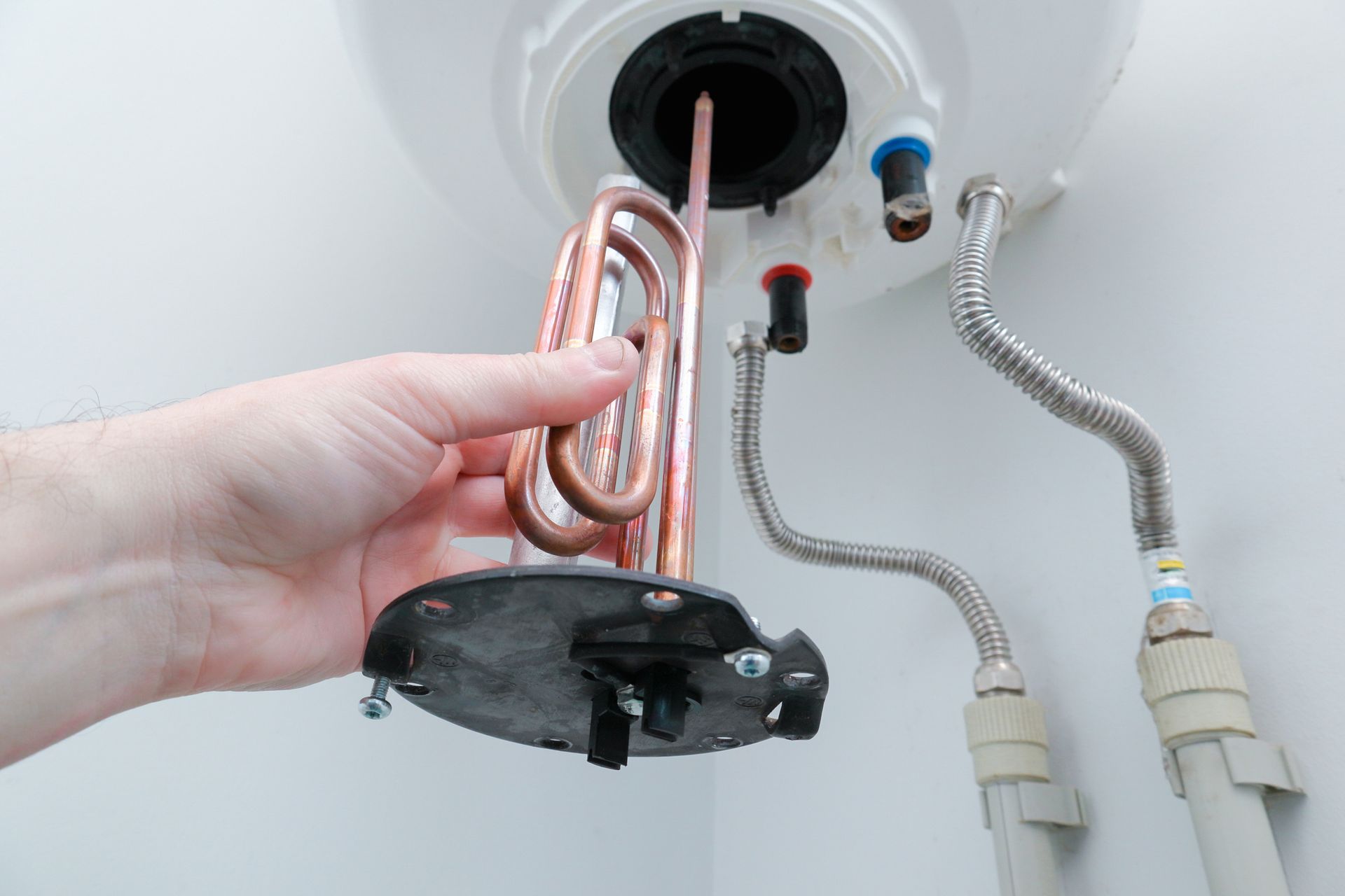 A person is holding a heating element in their hand in front of a water heater.