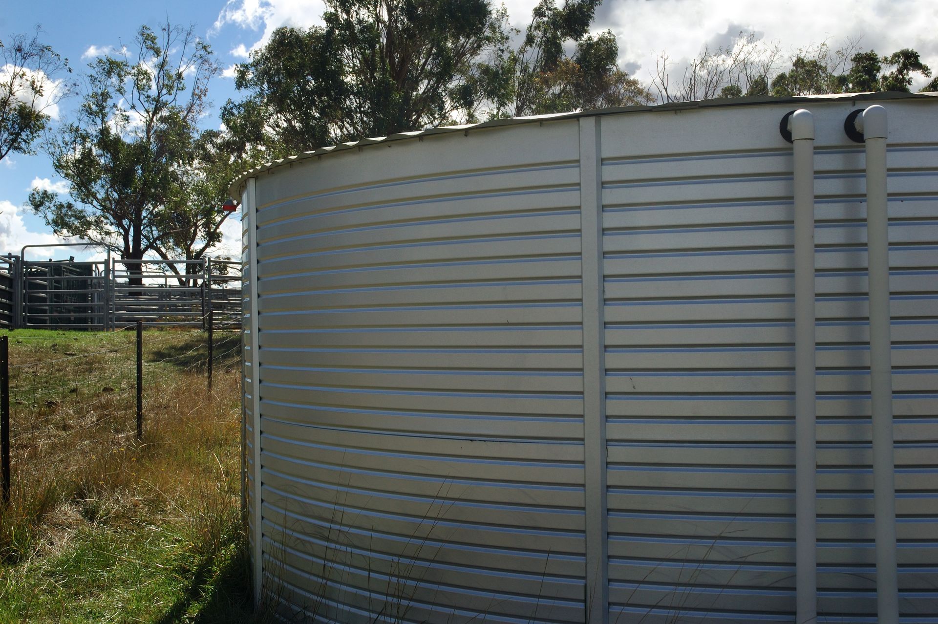A large metal cylinder is sitting on the side of a road next to a grassy field.