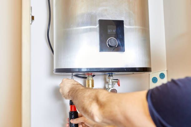 A man is fixing an electric water heater with a screwdriver.