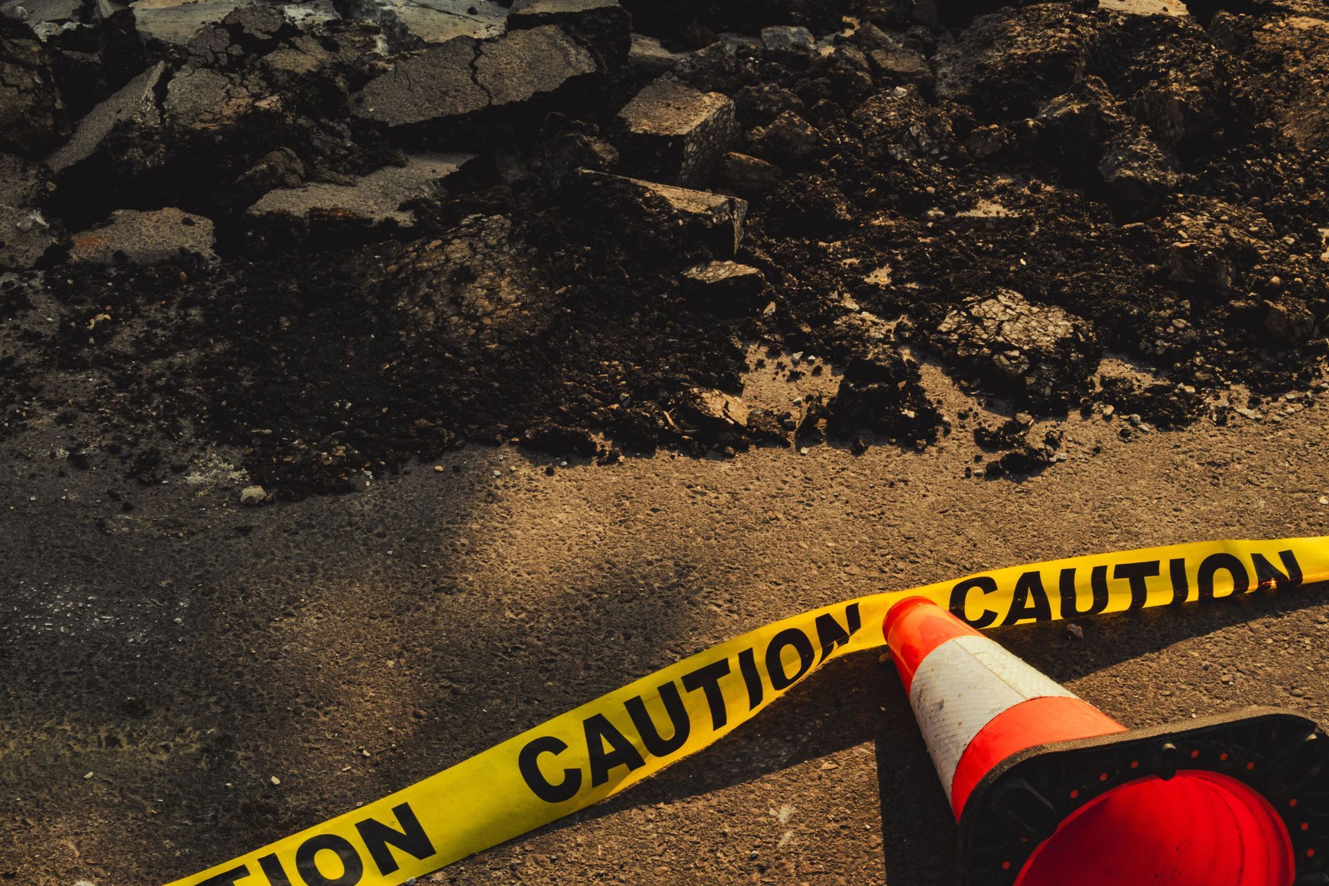 Caution tape and a traffic cone marking a damaged, debris-strewn road surface