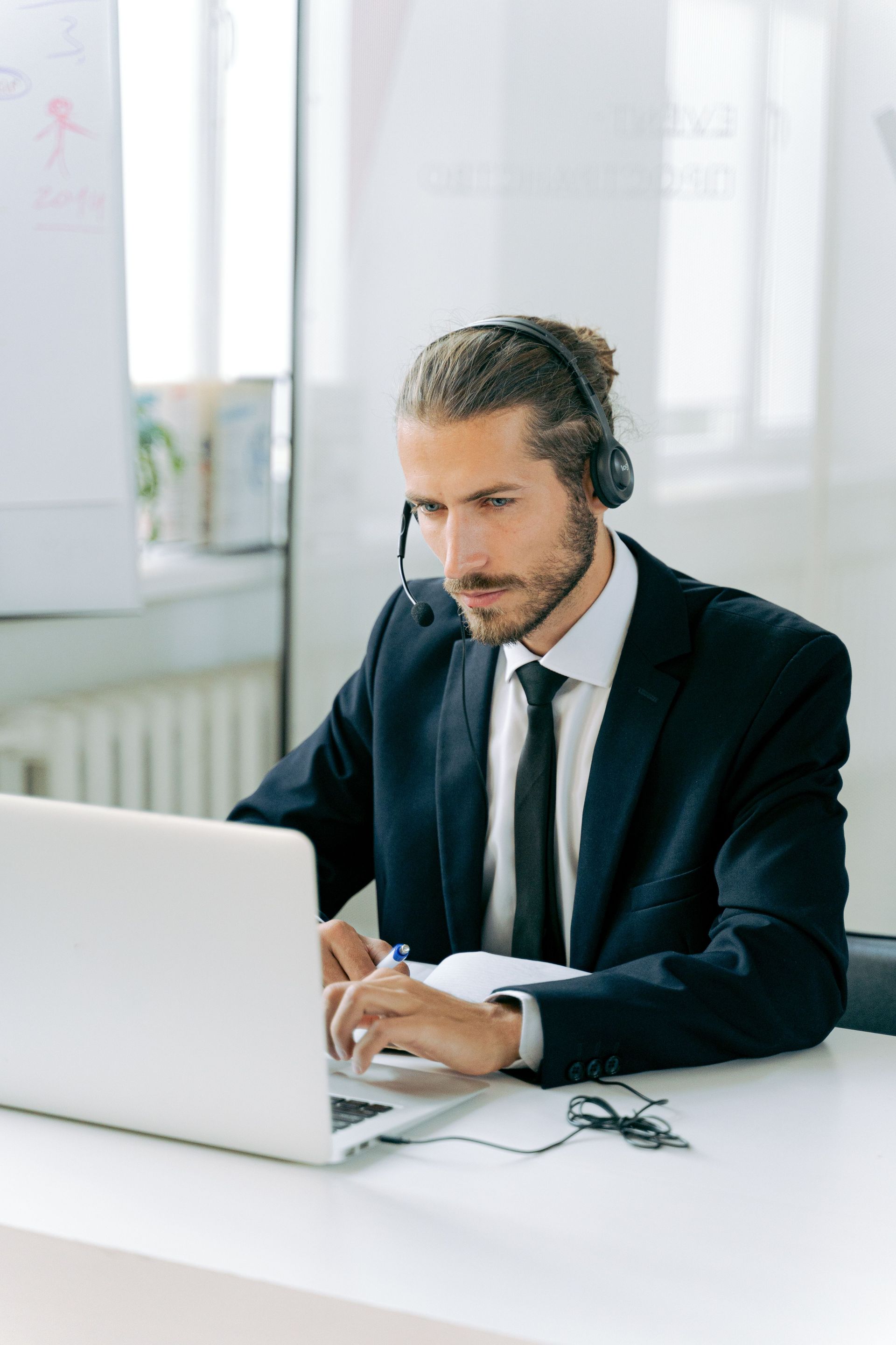 Man in a dark suit working on a laptop at a bright office desk