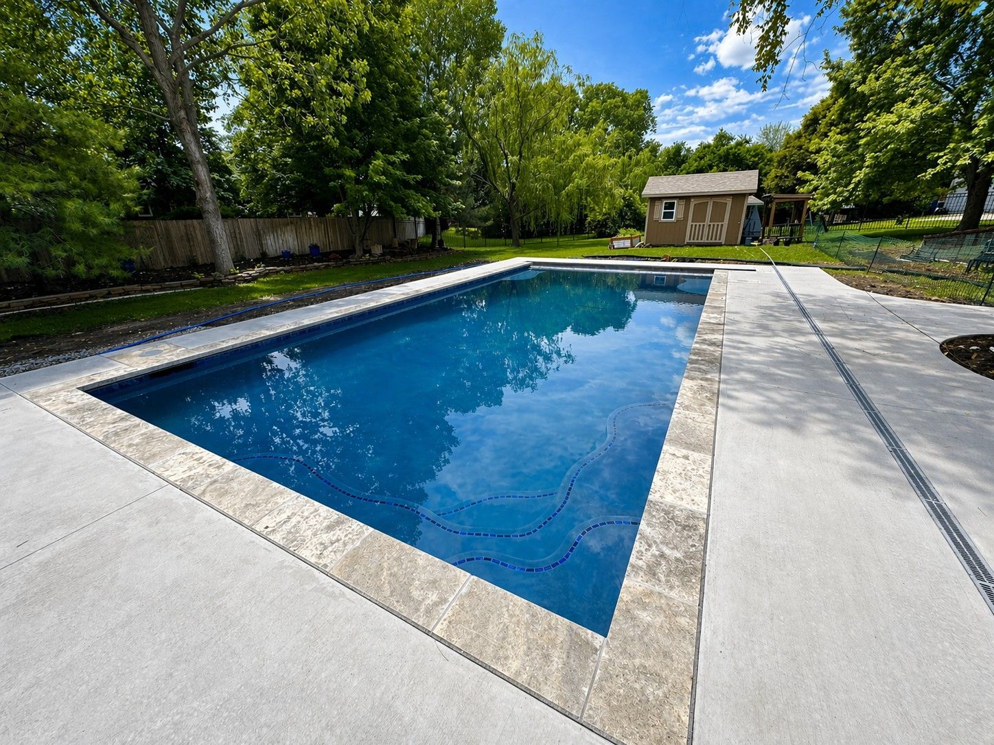 Backyard swimming pool with blue water, white deck, and trees surrounding it