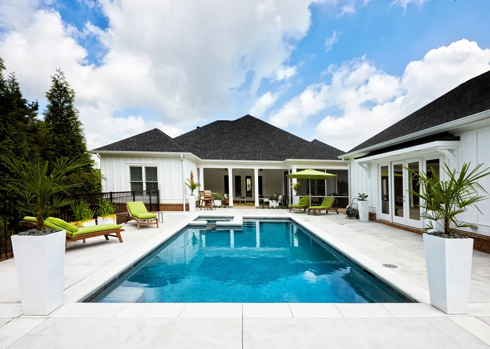 Modern white villa with a turquoise swimming pool and patio chairs under a blue sky