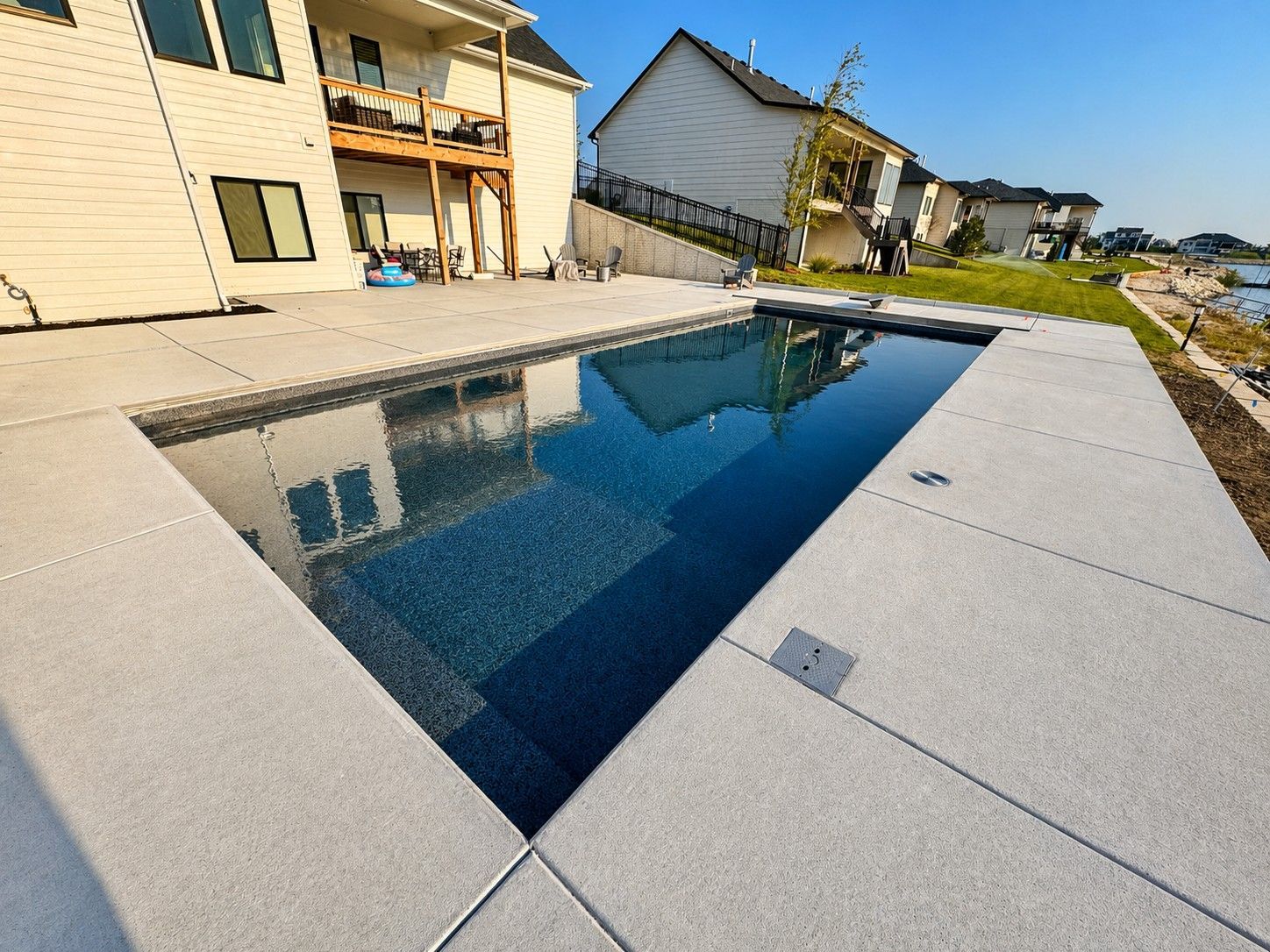 Modern backyard pool with dark blue water beside a house and paved patio in bright sunlight