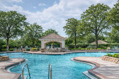 Picture of a curvy blue pool with green trees and white puffy clouds