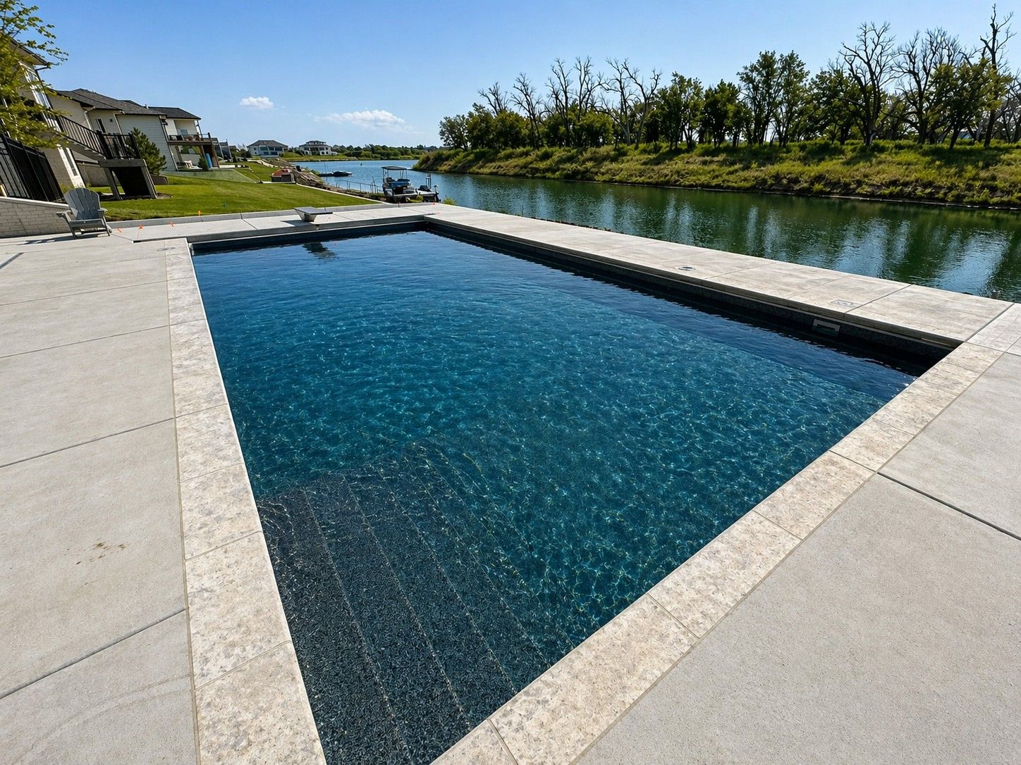 Modern rectangular pool beside a canal with stone deck and blue water on a sunny day